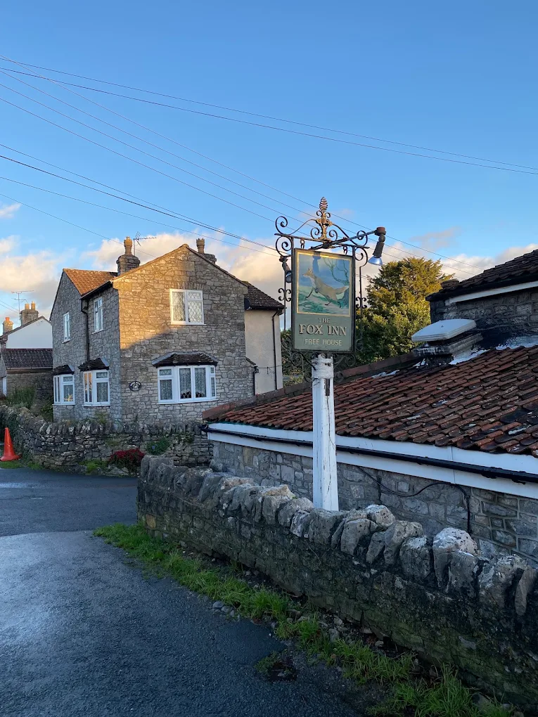The Fox Inn sign and stone cottages in low winter sunlight from the lane