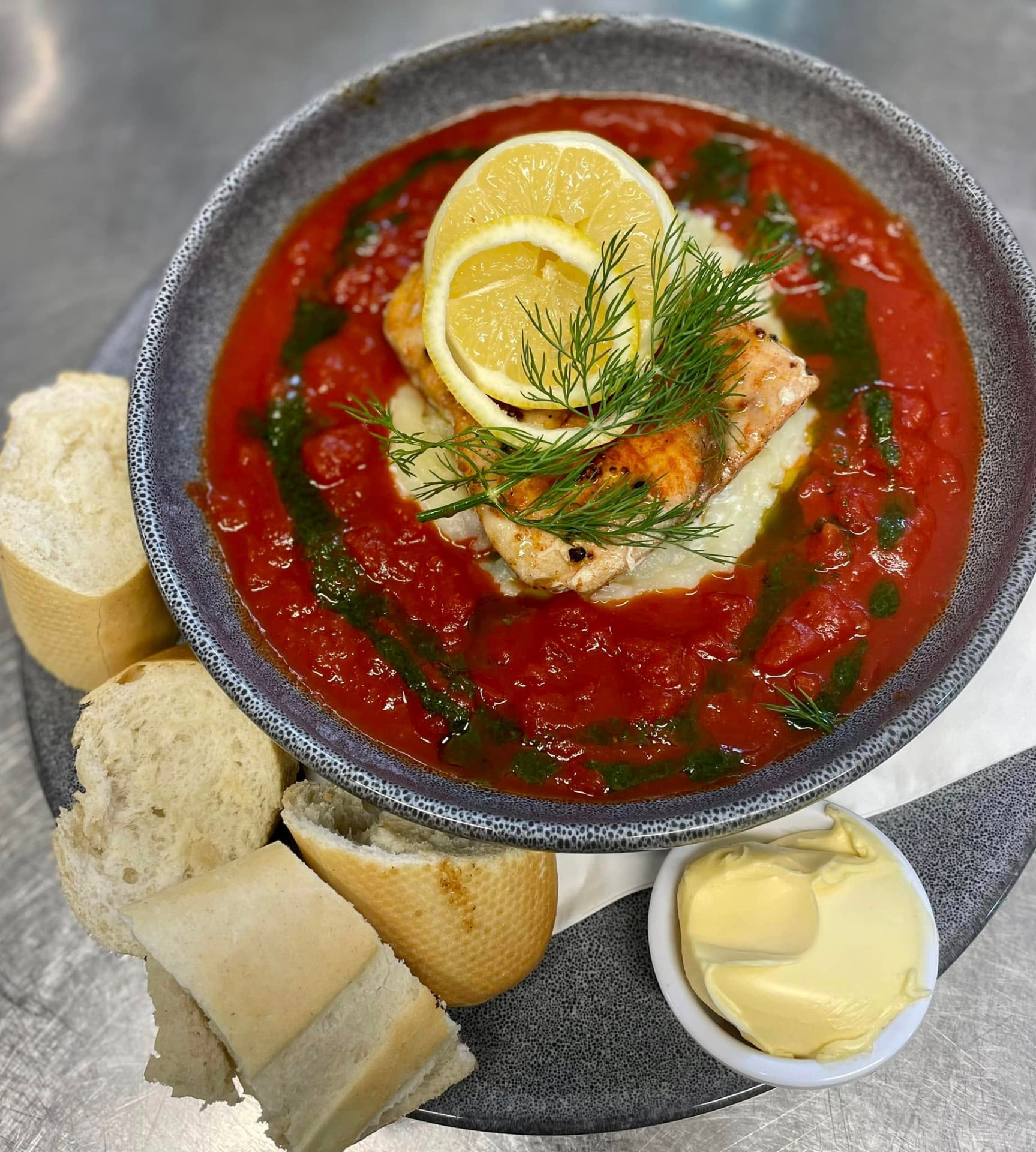 Pan-seared salmon on mash in a rich tomato sauce, served with crusty bread