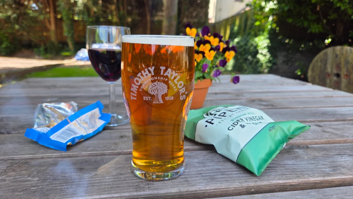 A pint of Timothy Taylor's and crisps on a sunlit garden table