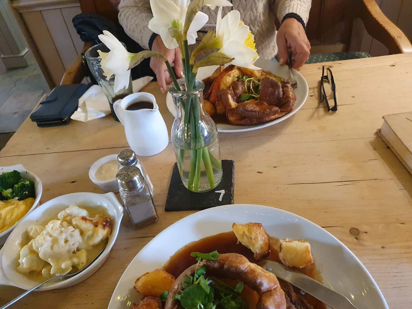 A Sunday roast with Yorkshire puddings, cauliflower cheese and gravy on a pine table