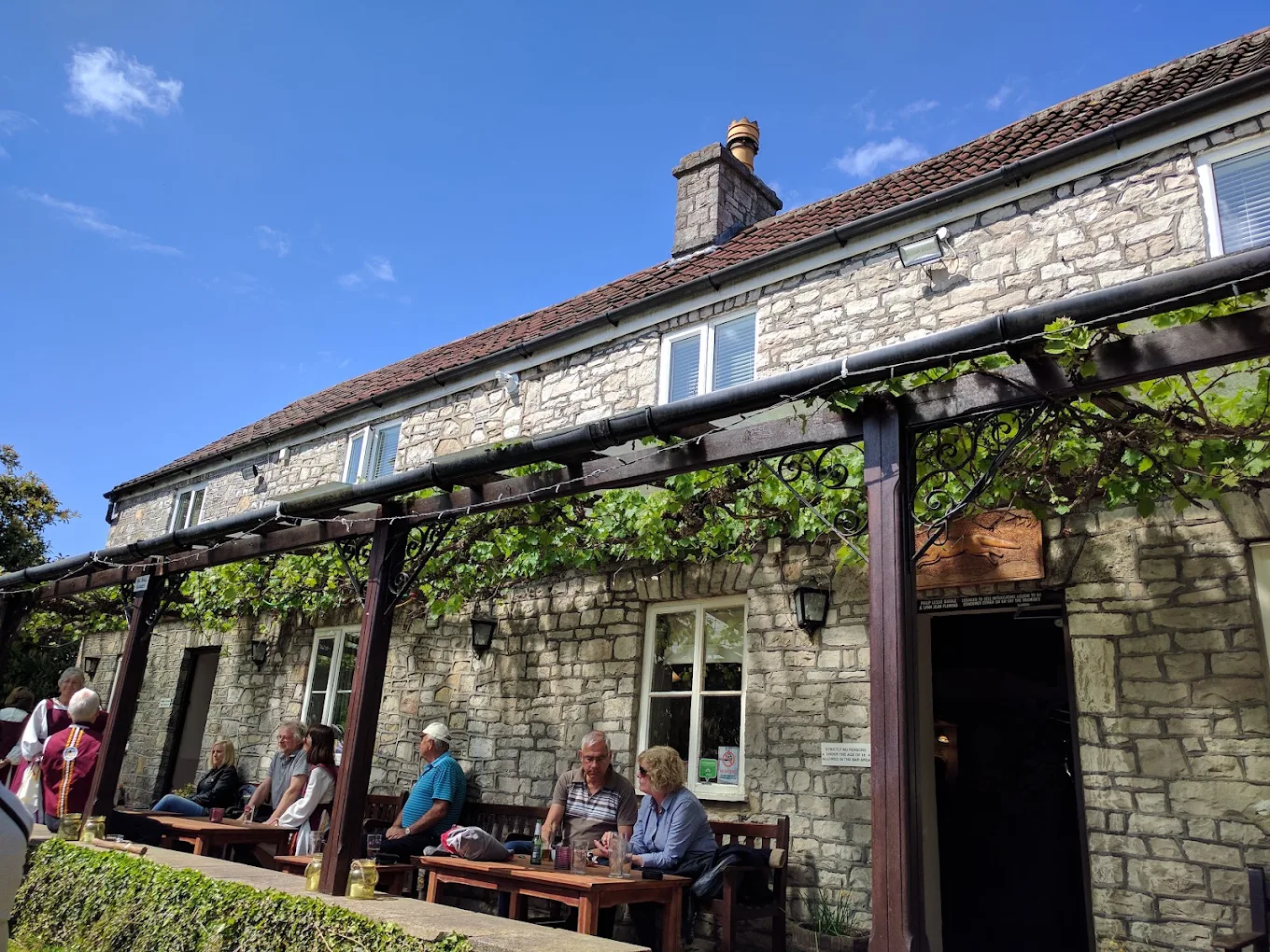 The stone frontage of The Fox Inn with vines over the veranda under a blue sky