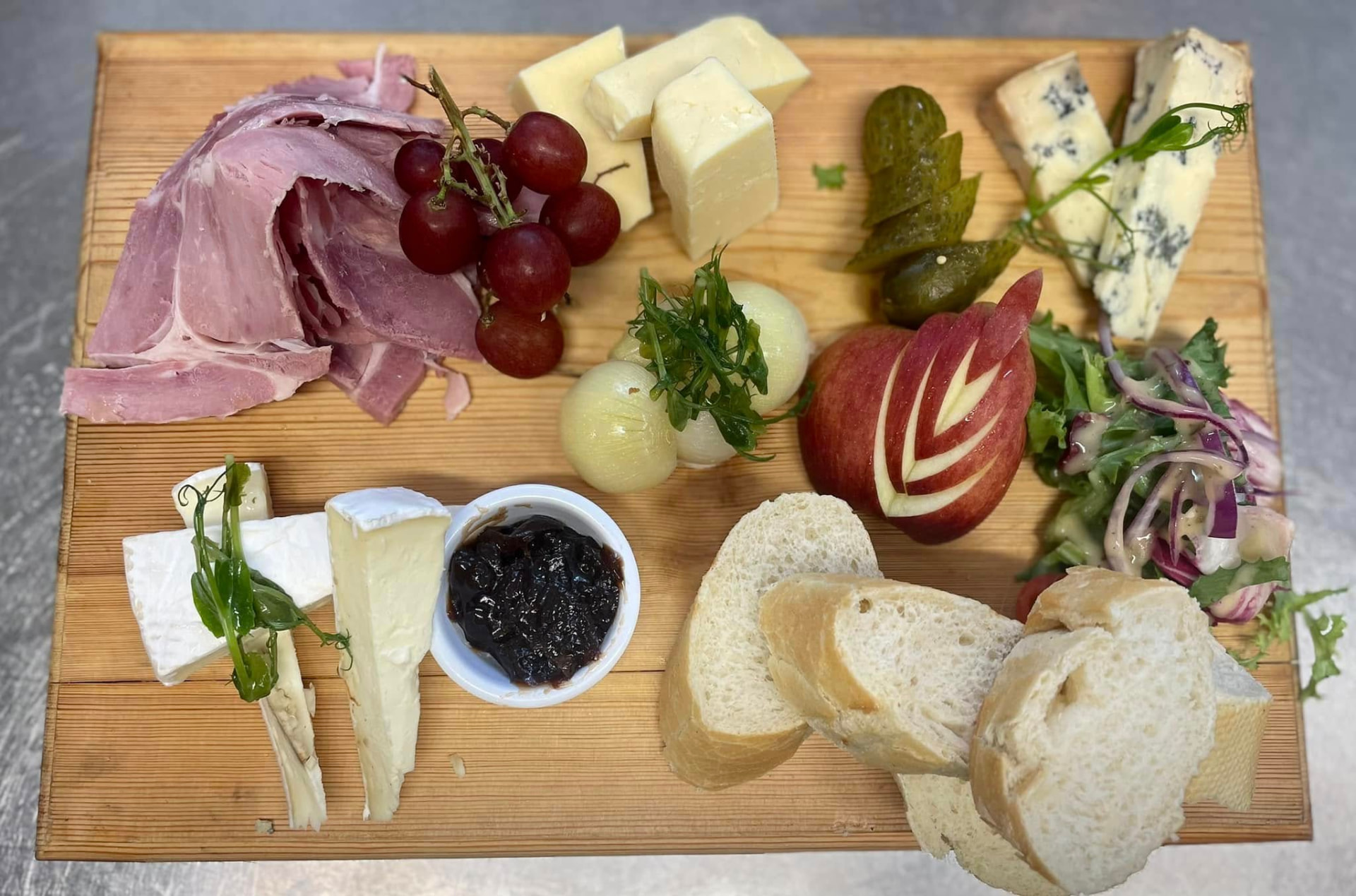 A sharing board of ham, cheeses, chutney, salad and fresh bread
